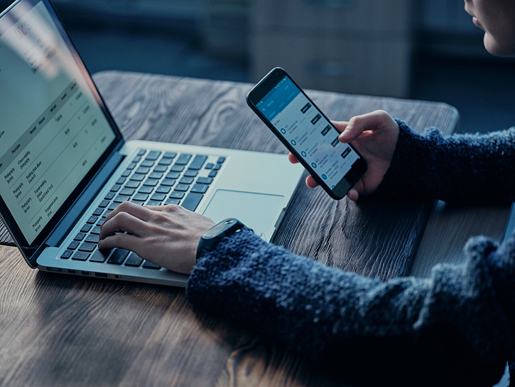 A man types on a laptop with one hand and holds a smartphone in the other.